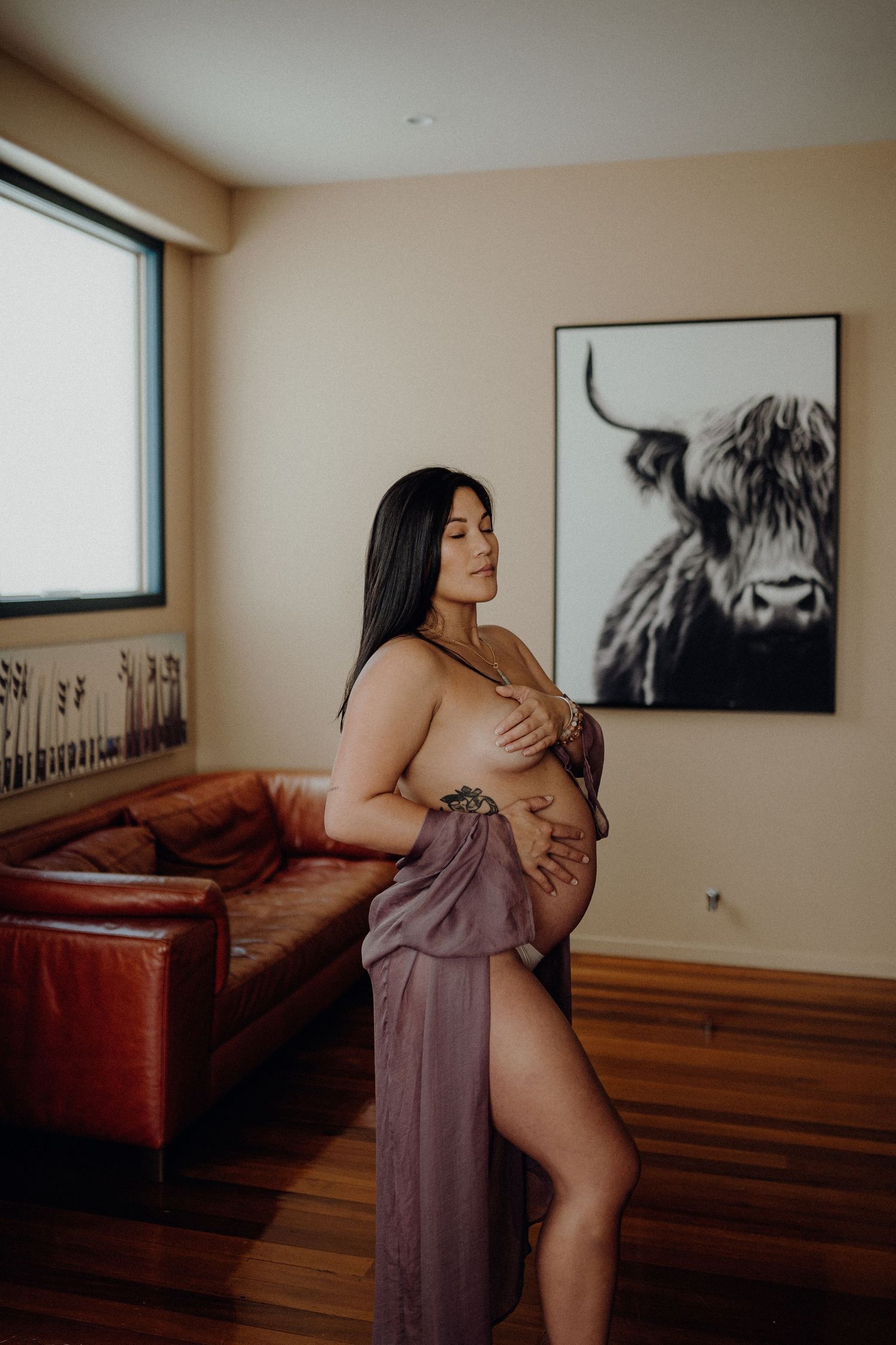 Intimate maternity boudoir photo in a modern room with a Highland cow artwork on the wall.