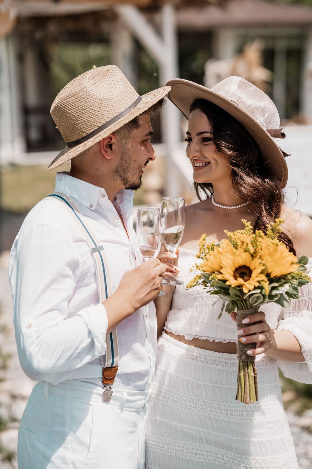 A couple in white outfits share a romantic moment while holding a sunflower bouquet.