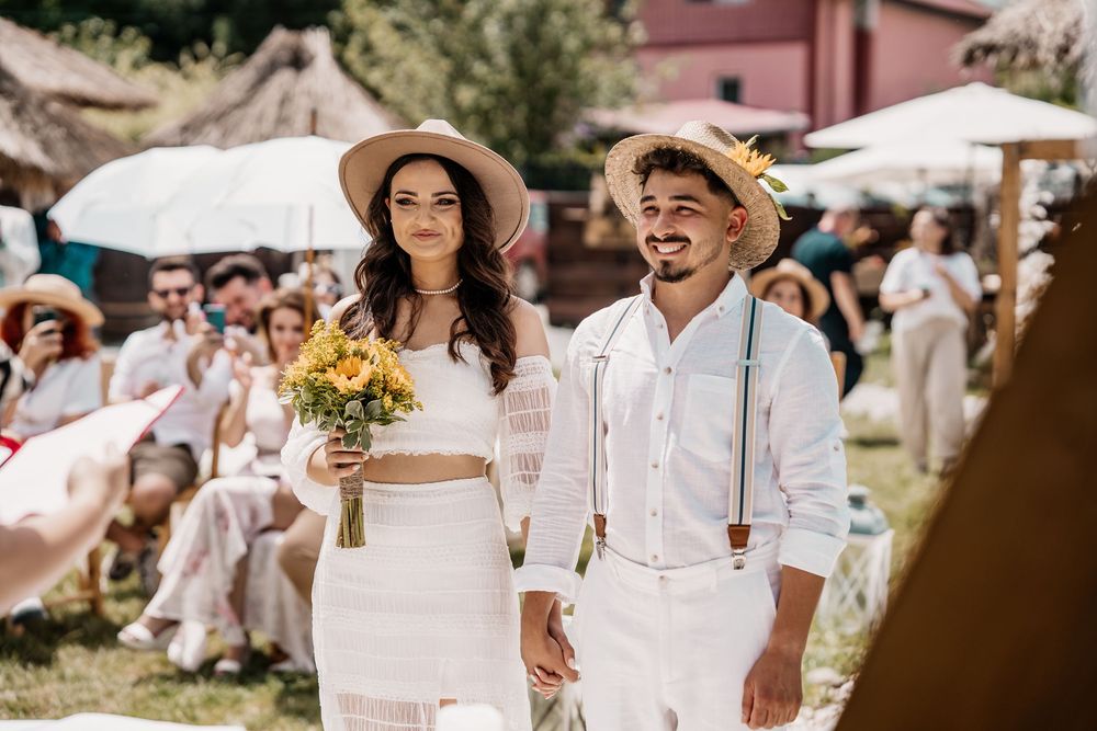 Couples and guests dressed in white mingle at a sunlit outdoor party with rustic decor.