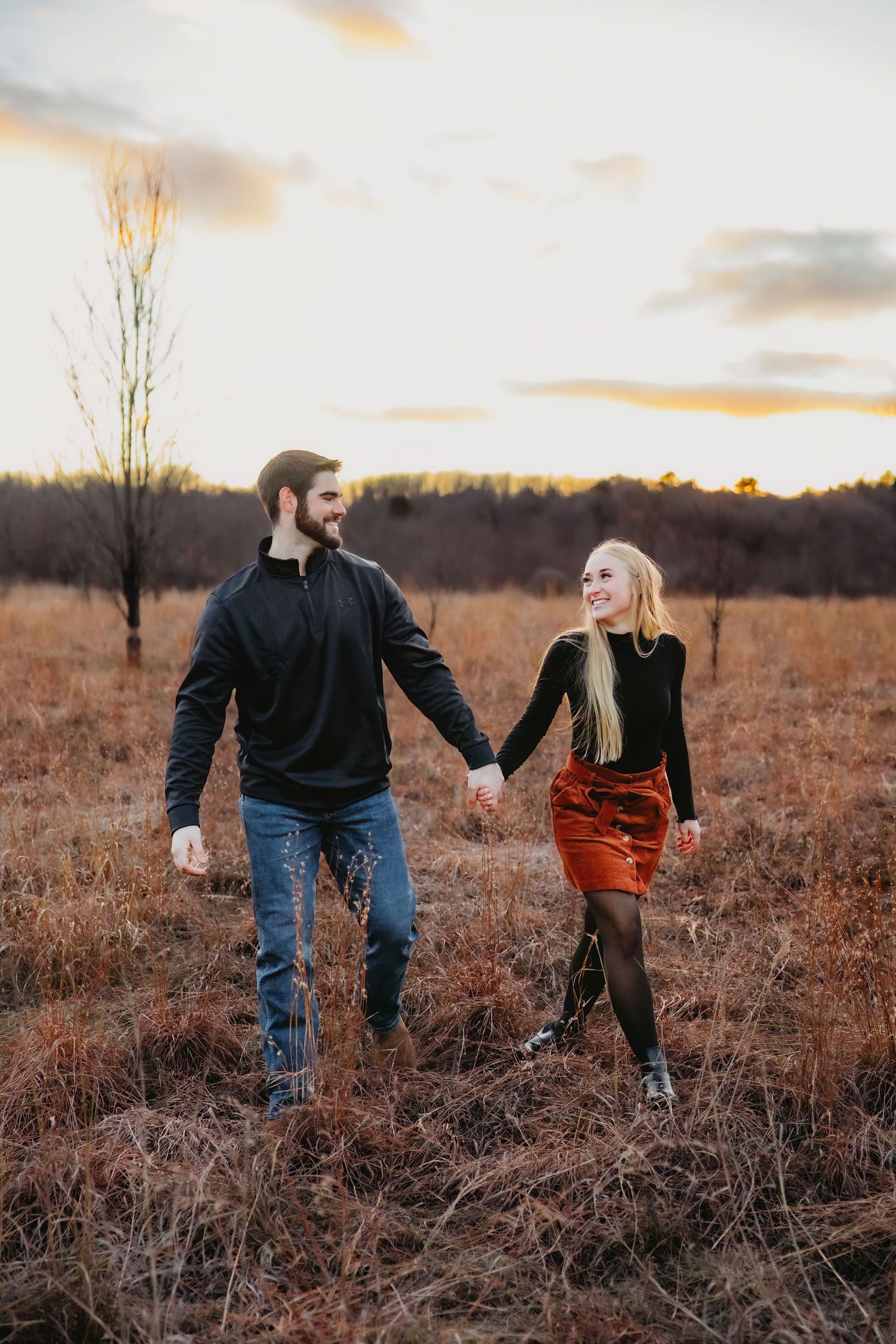 Couple walking through a golden autumn field at sunset holding hands.