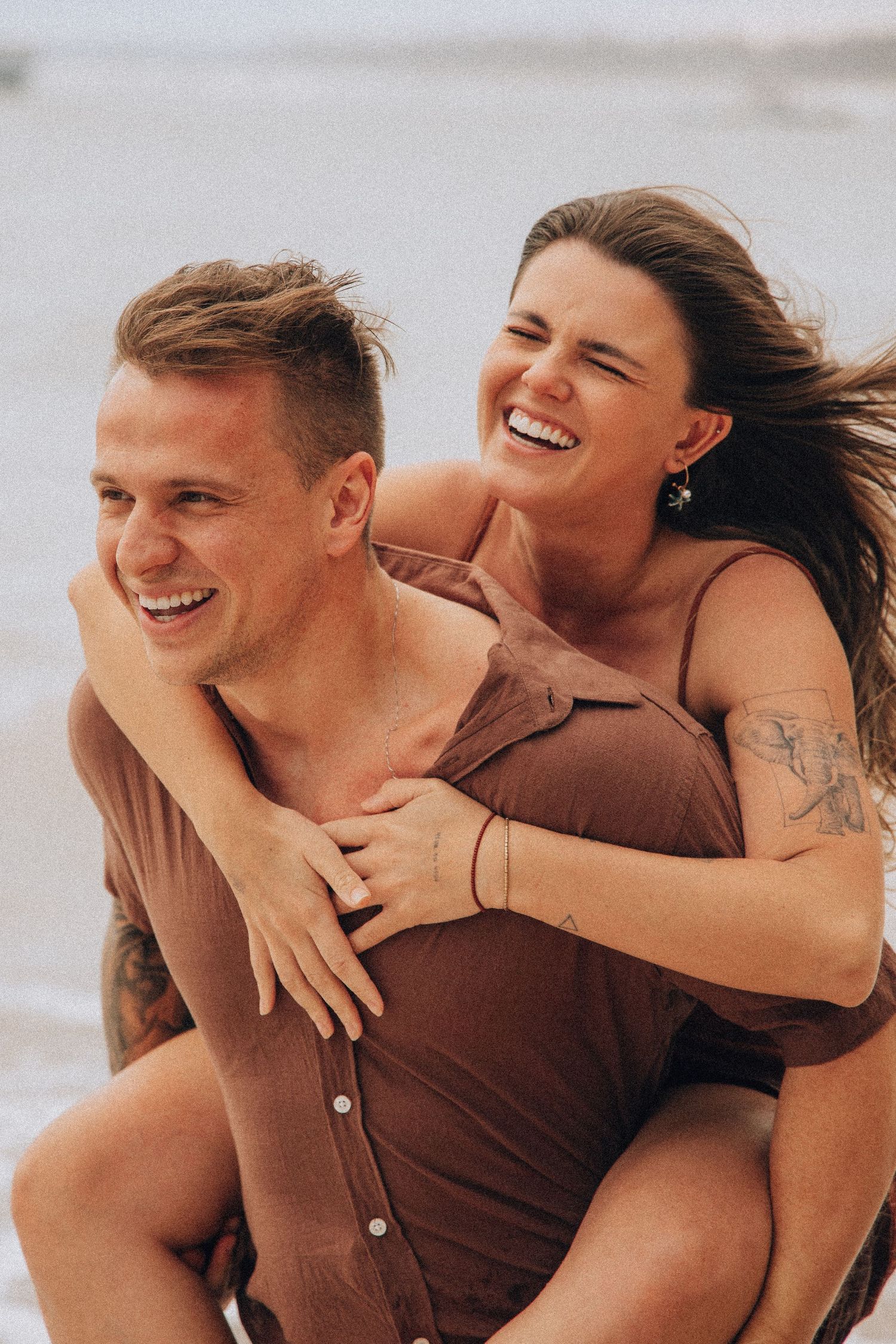 Happy couple laughing at the beach, woman riding piggyback on mans back.