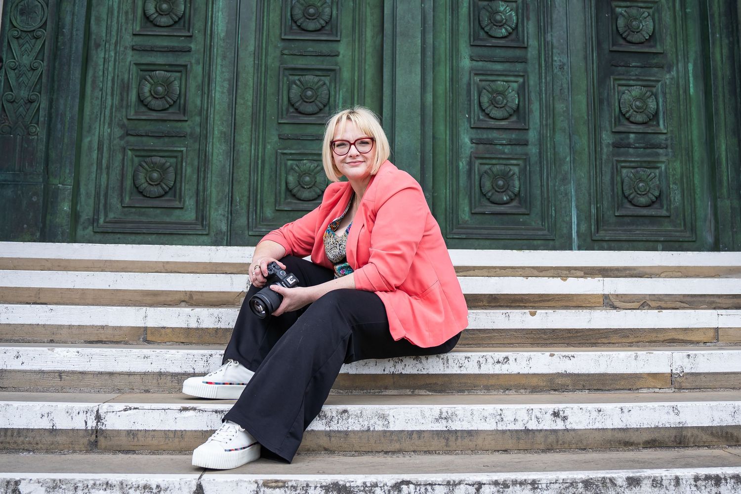 A person wearing leopard print and glasses smiles warmly at camera in restaurant setting.