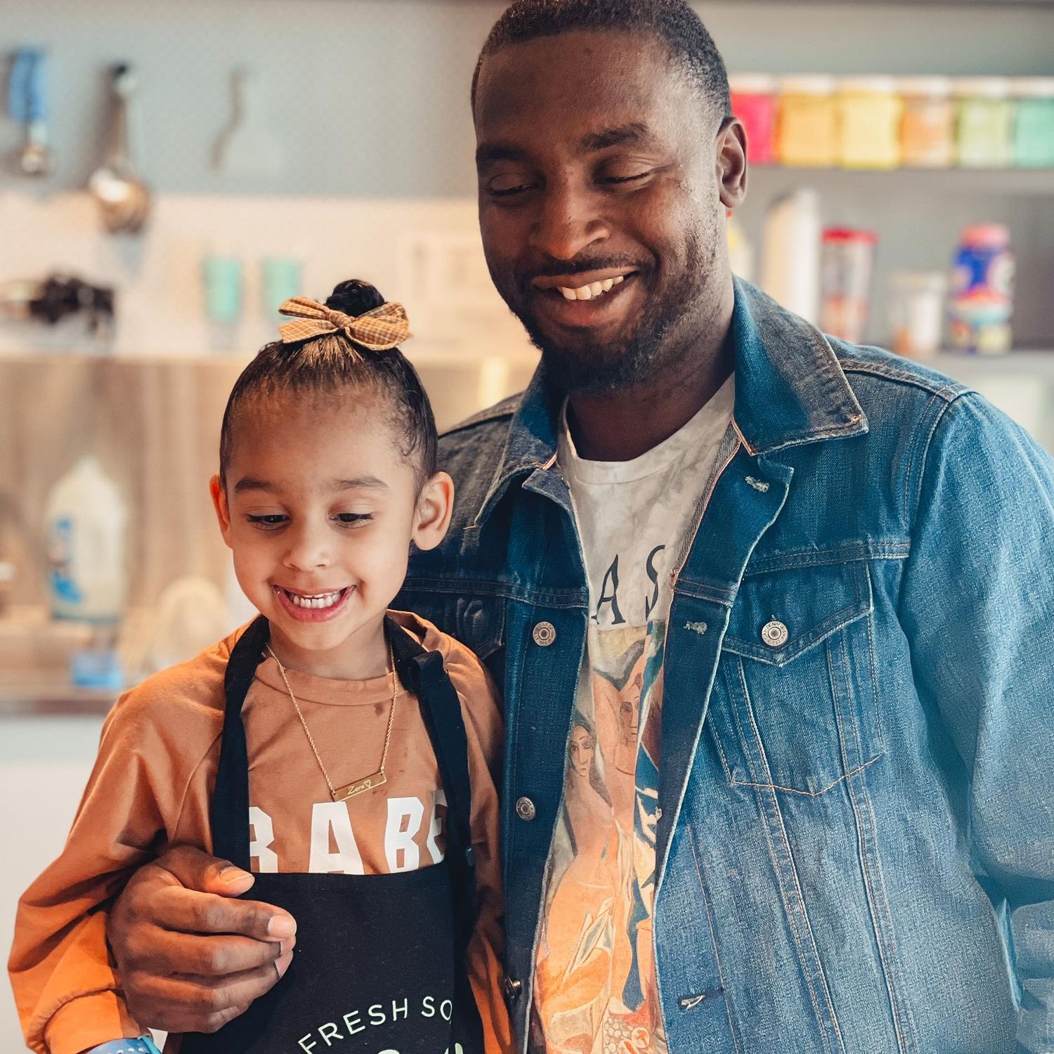 Smiling man and young girl wearing aprons together in a bright colorful kitchen setting.