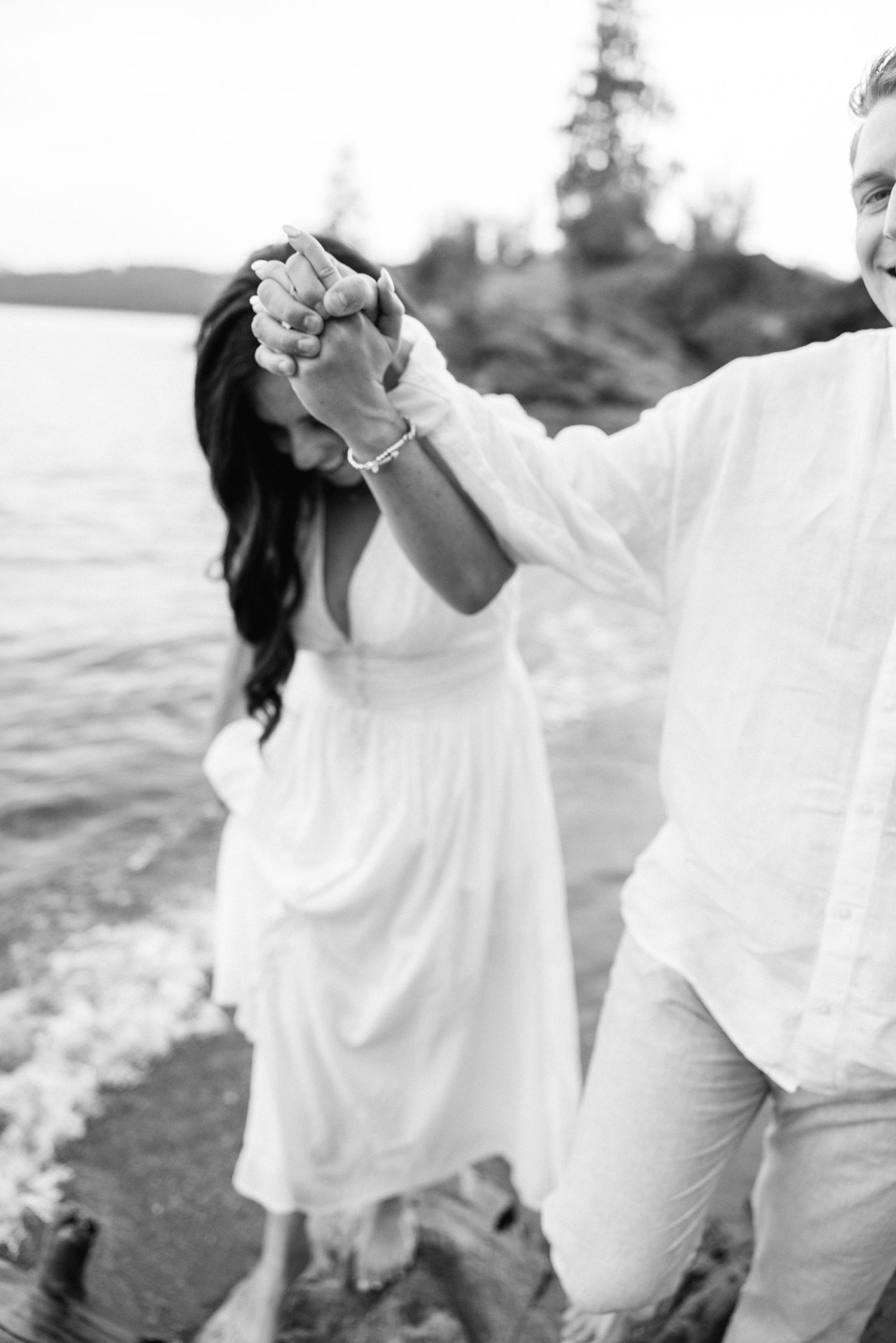 Black and white photo of couple dancing and holding hands at the water's edge.