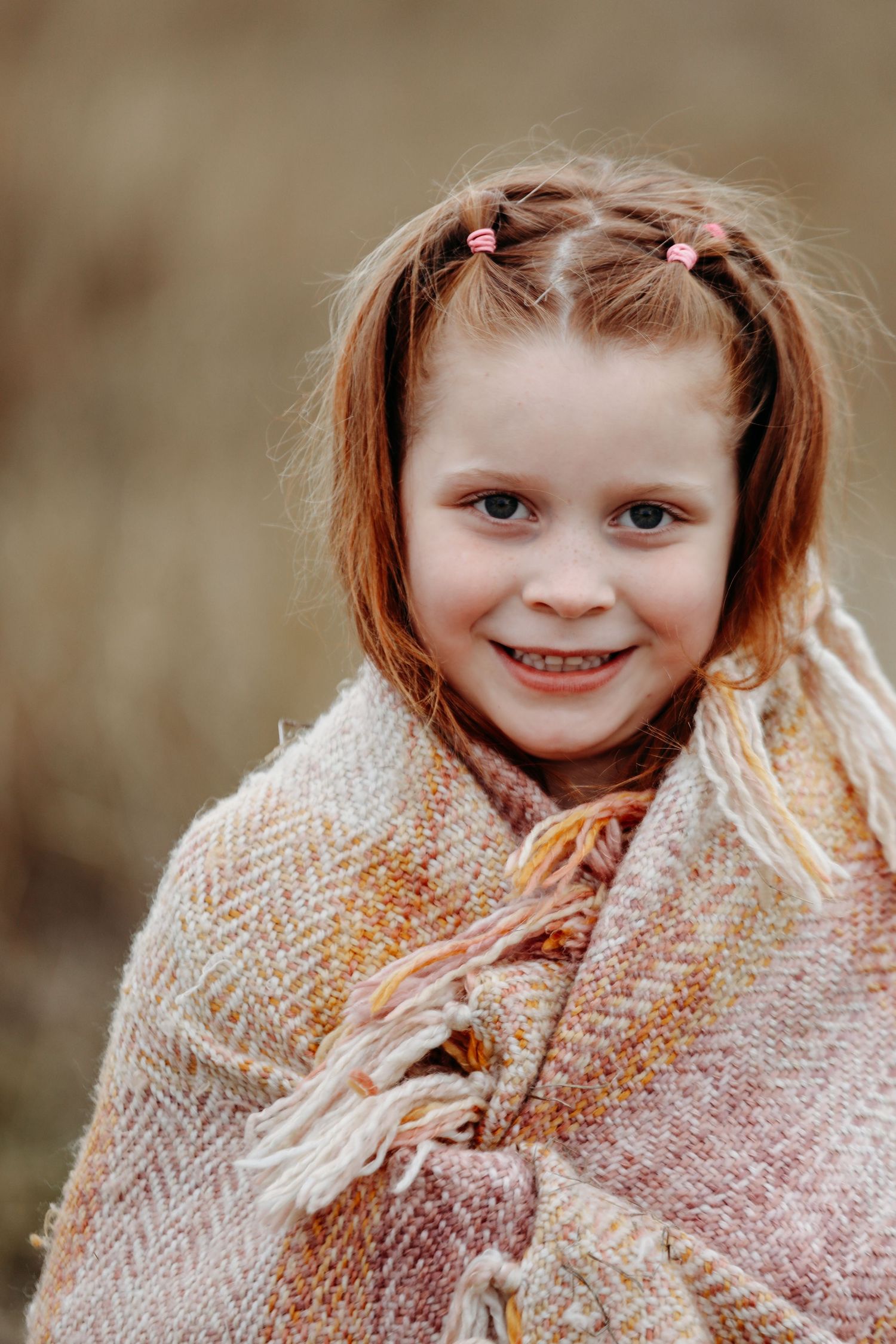 Young child wrapped in textured beige blanket smiling at camera.