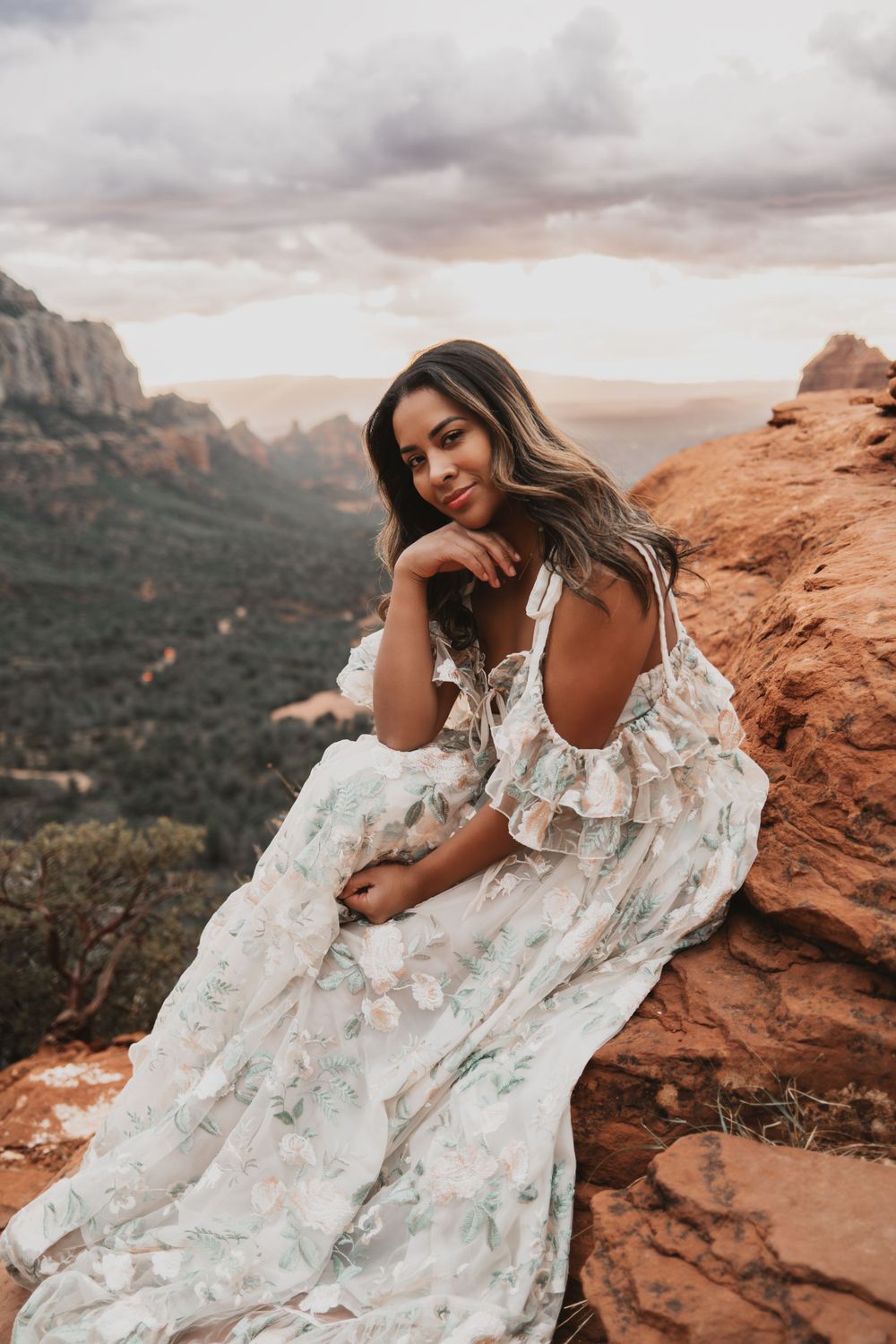 Elegant white dress flows in the wind atop red rock formations with mountain vista backdrop.