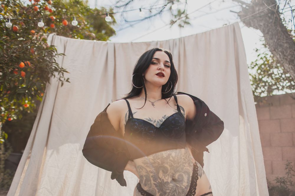 Model in black lingerie poses elegantly against white backdrop with orange florals in background.