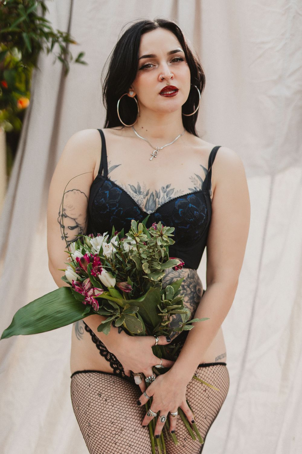 Model in black attire holds bouquet of flowers and greenery against light backdrop.
