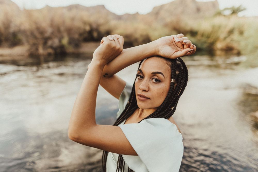 Portrait at riverside with desert mountains and warm sunset lighting.