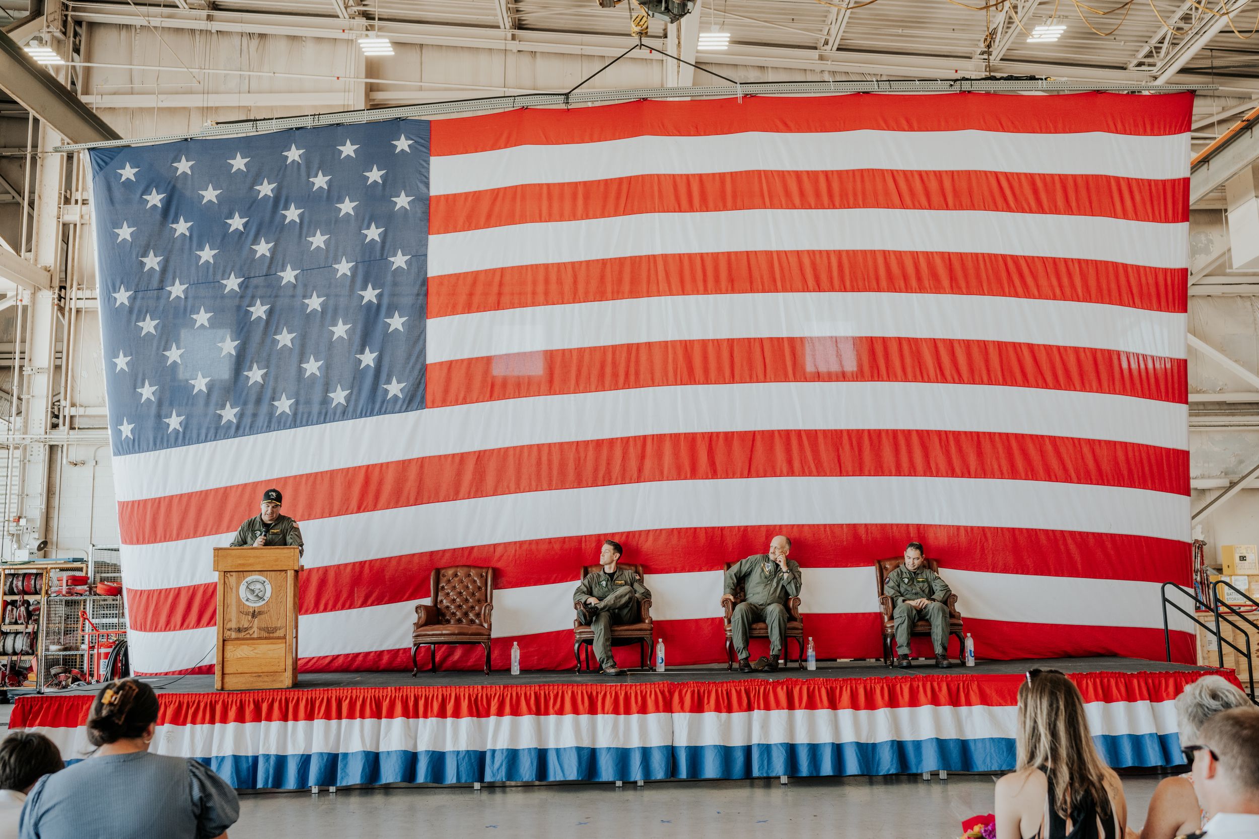 A large American flag serves as backdrop for a panel discussion set up on a stage with red white and blue bunting.