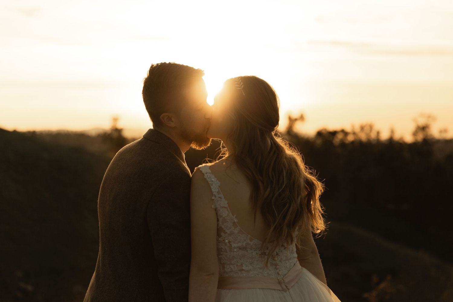 Romantic couple silhouetted kissing against stunning golden sunset in outdoor landscape.