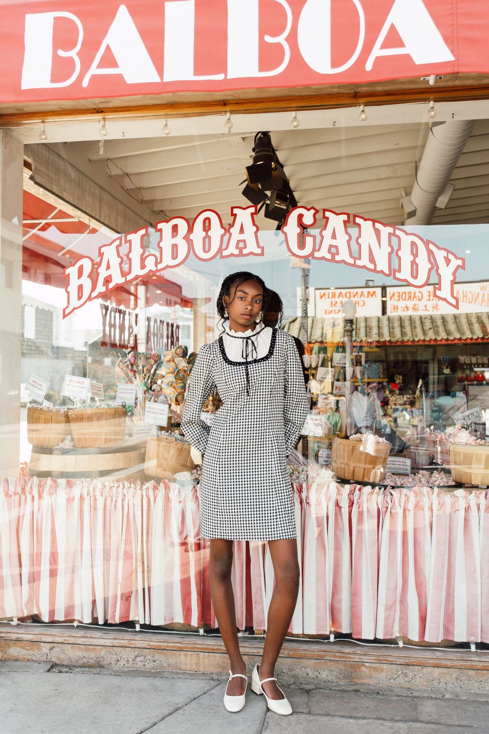 Black model standing in front of vintage candy shop in gingham dress, Atlanta editorial portrait and fashion photographer
