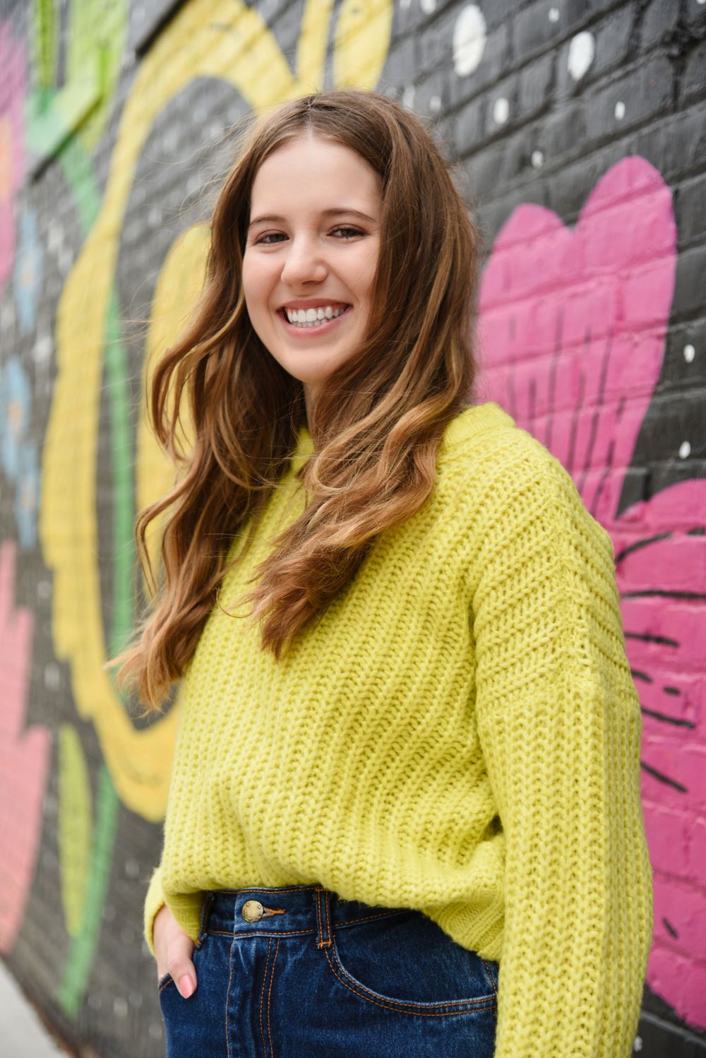 Yellow knit sweater styled against colorful graffiti wall background.