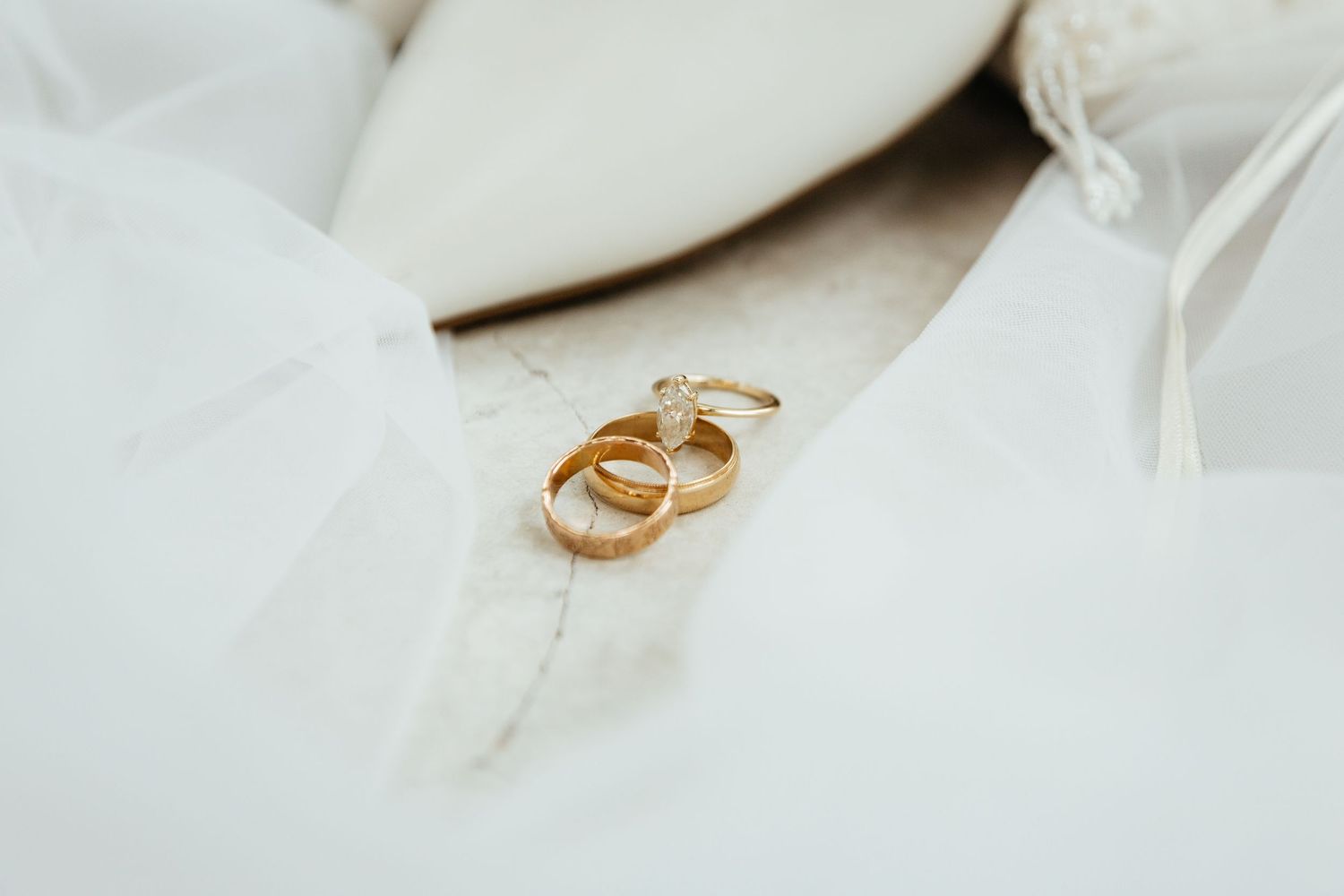 Gold wedding rings and diamond engagement ring displayed on white quilted bridal pillow with shoes and perfume.