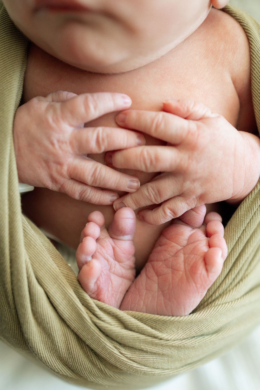 Close-up of a newborn baby's tiny hands and feet wrapped in a soft green swaddle blanket.