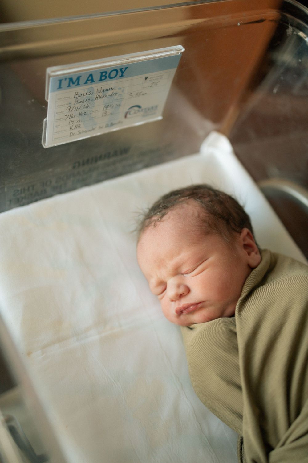Newborn baby boy sleeping in hospital bassinet with I'm a Boy identification card.