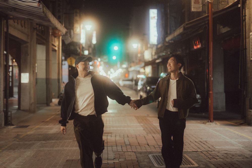 Two people holding hands on a brick street at night with city lights glowing in the background.