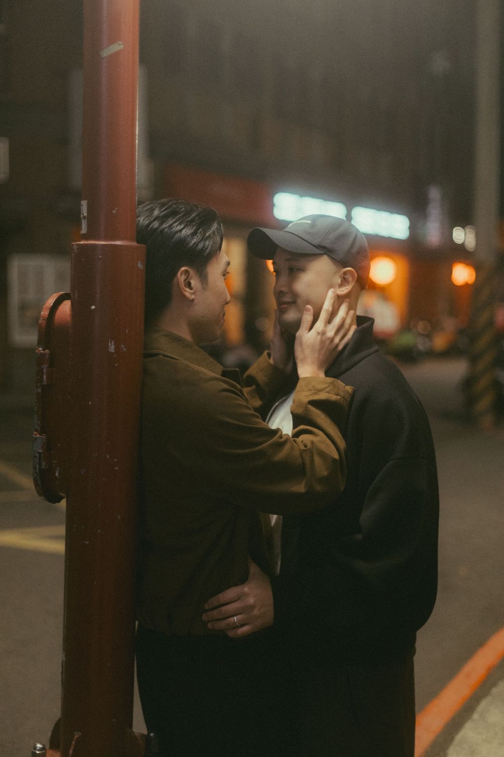 Two people share an intimate moment near a street pole at night in a city.