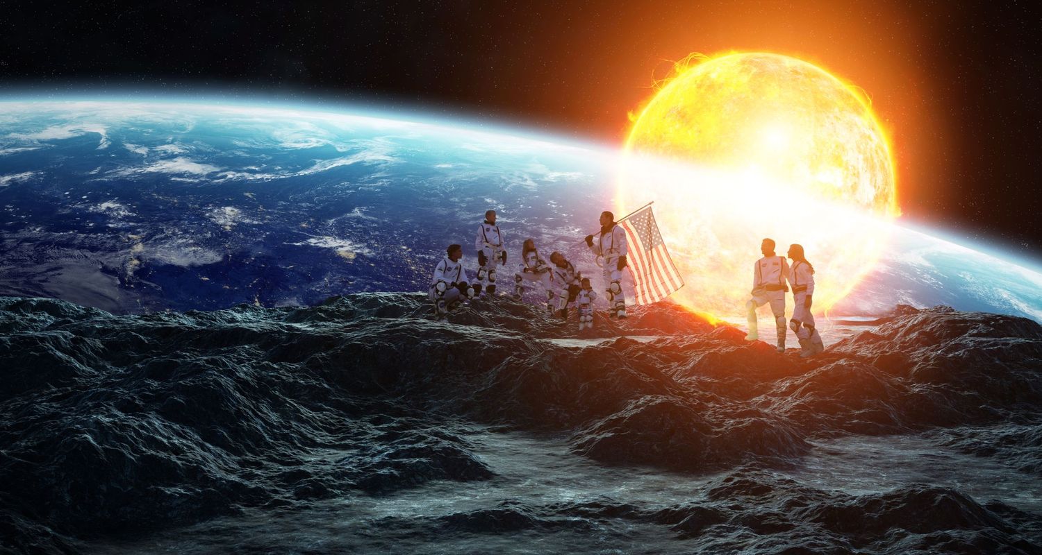 Astronauts stand on a rocky lunar surface beside an American flag as a bright sun rises over Earth.