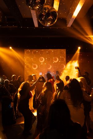 People dancing in a nightclub with golden lighting, disco ball, and circular pattern backdrop.
