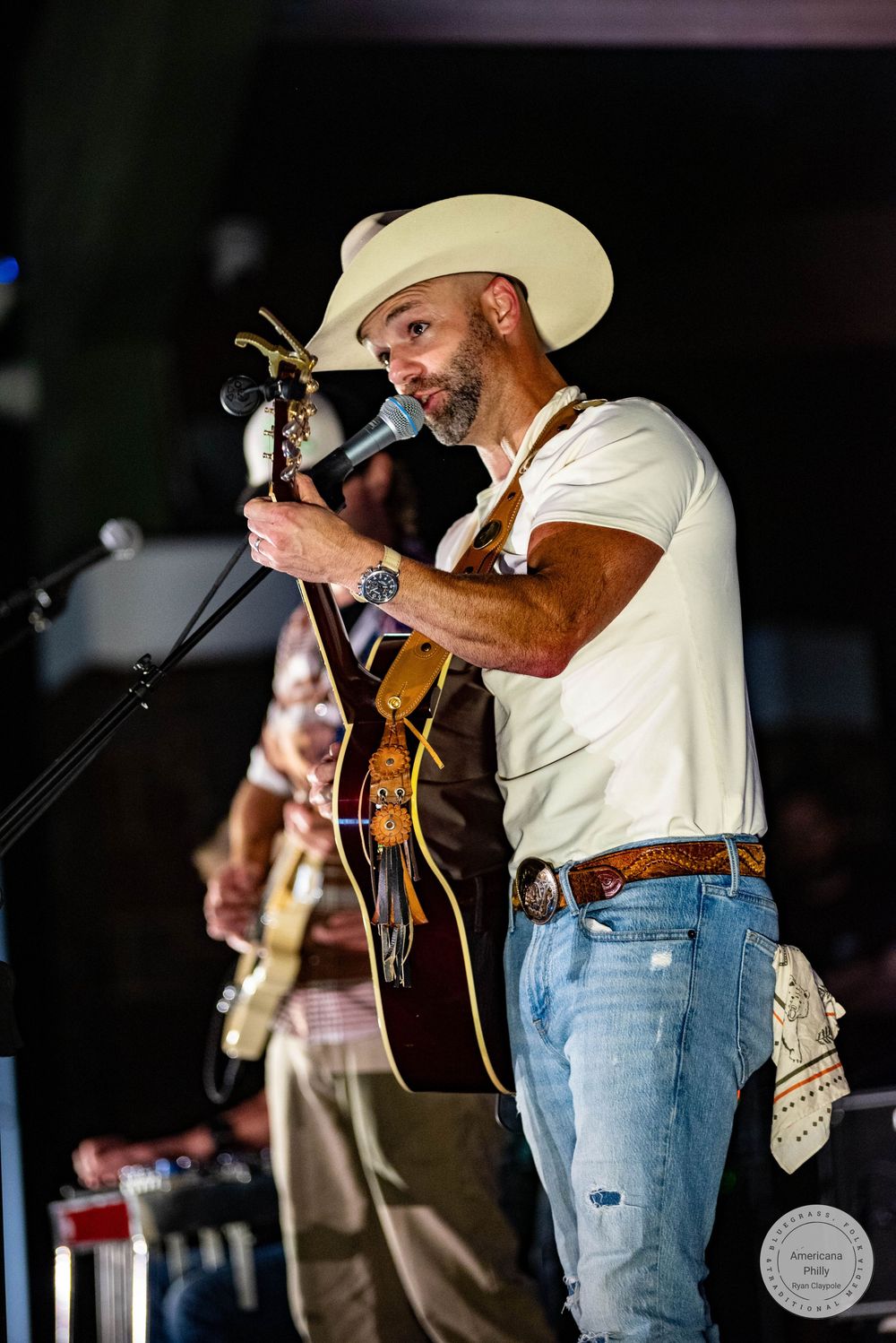 Male country singer in white shirt and cowboy hat playing acoustic guitar on stage at night.