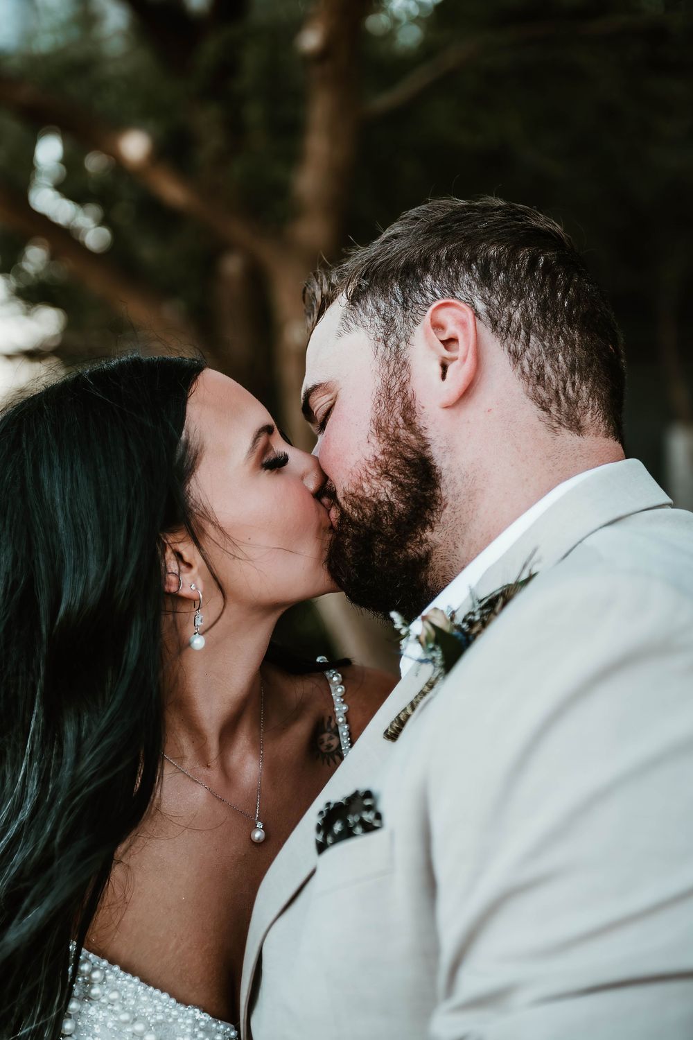 A bride and groom share a romantic kiss, with the groom in a white suit and boutonniere and the bride in a sparkly dress.