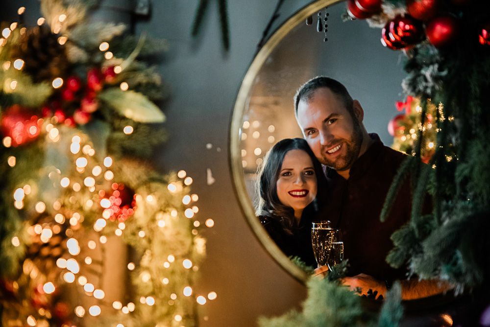 karácsonyi fotózás, páros
Couple smiling in mirror reflection surrounded by Christmas tree lights and holiday decorations.