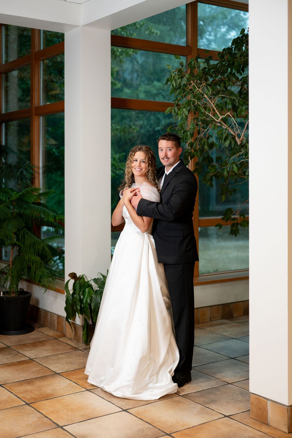 Bride and groom share a dance in an elegant indoor venue with large windows and lush green plants.