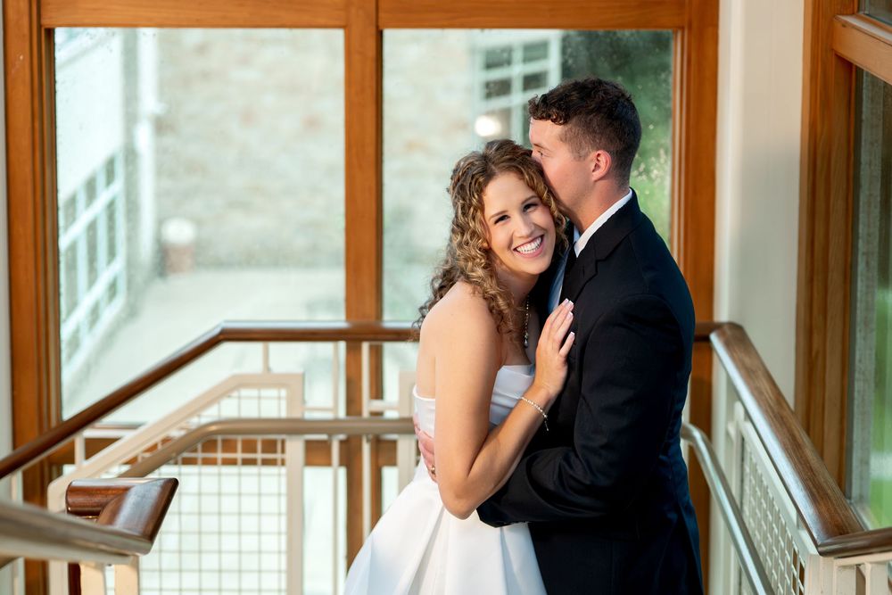 Bride and groom sharing a romantic moment on a staircase, groom kissing bride's cheek at a wedding venue.