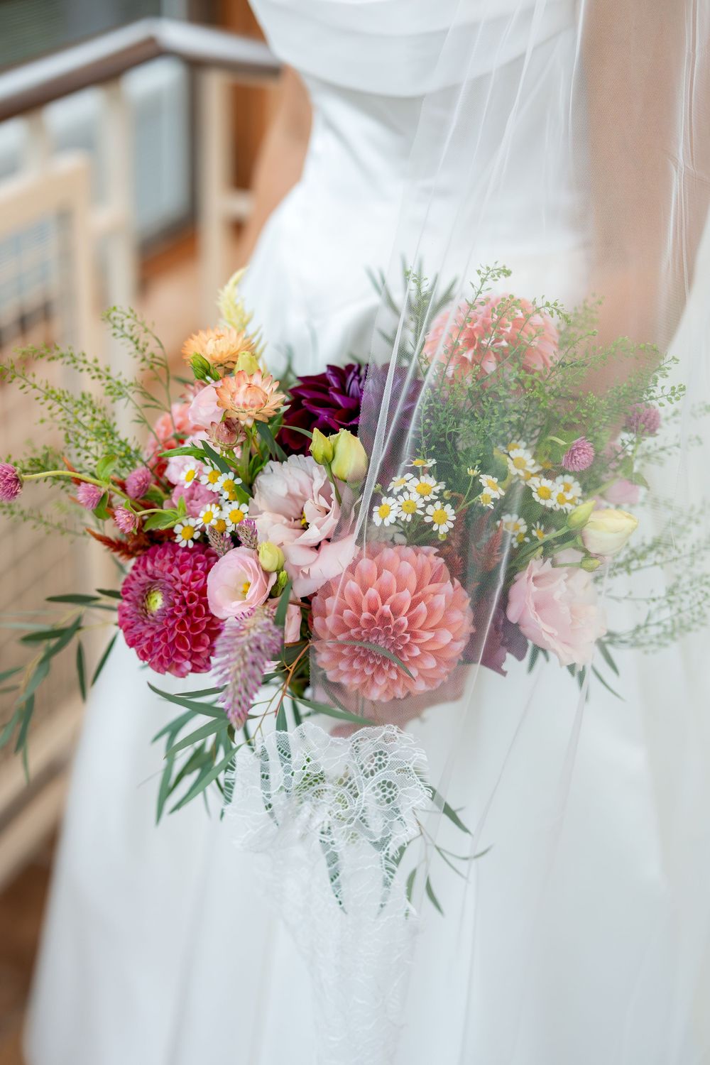 Bride holding a vibrant wedding bouquet with pink dahlias, roses, and wildflowers, wearing a white strapless gown and veil.