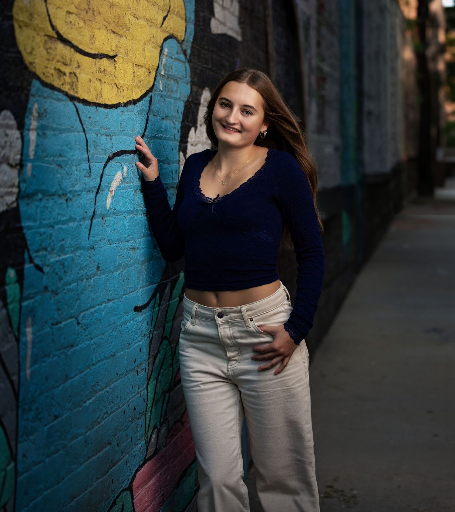 Senior portrait of a brunette girl photographed beside a colorful urban mural