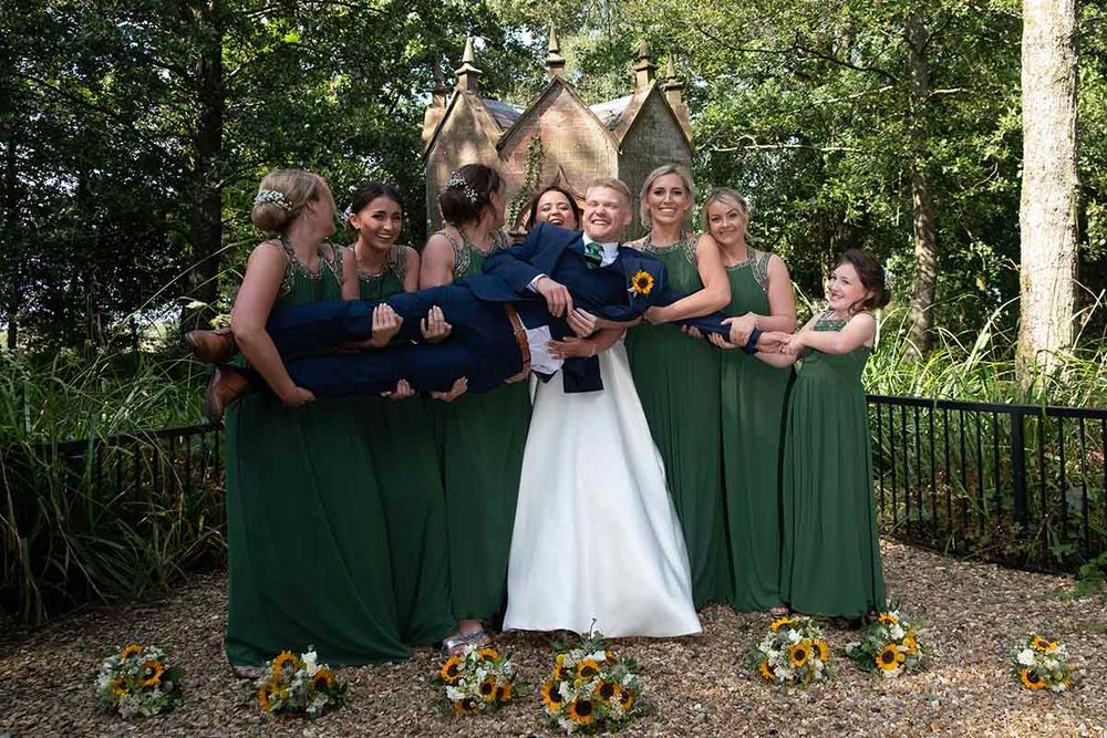 Bride in white gown surrounded by bridesmaids in green dresses lifting groom at Blaithwaite House Wigton Cumbria