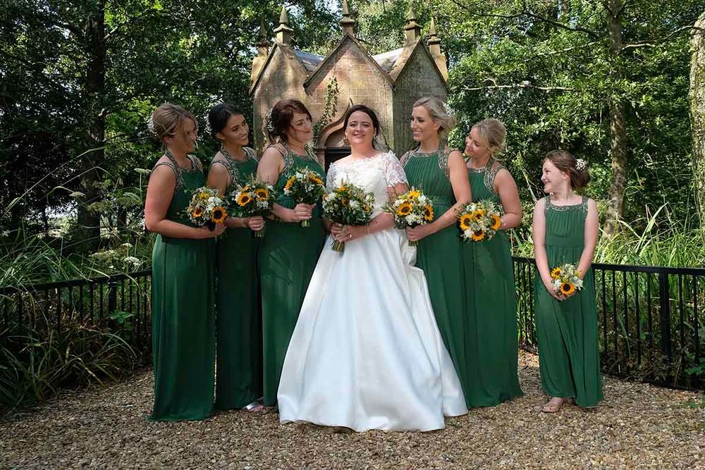 Bride in white gown with bridesmaids in emerald green dresses stand outside the chapel at Blaithwaite House wedding venue