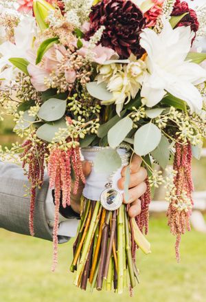 Elegant bridal bouquet with burgundy dahlias, white lilies, pink blooms, and cascading amaranthus tied with a decorative charm.