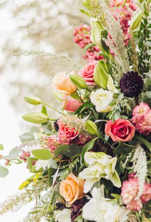 Lush floral arrangement featuring pink roses, orange blooms, white lilies, and greenery in a elegant wedding display.