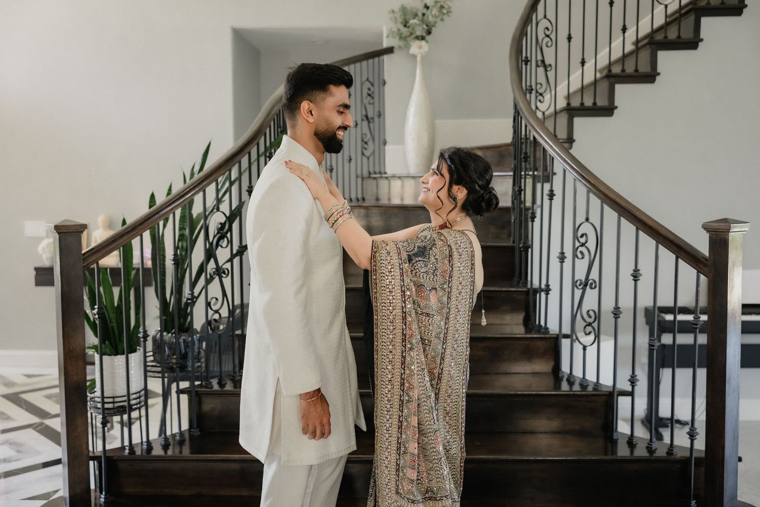 Couple in traditional South Asian wedding attire sharing a tender moment on an elegant staircase.