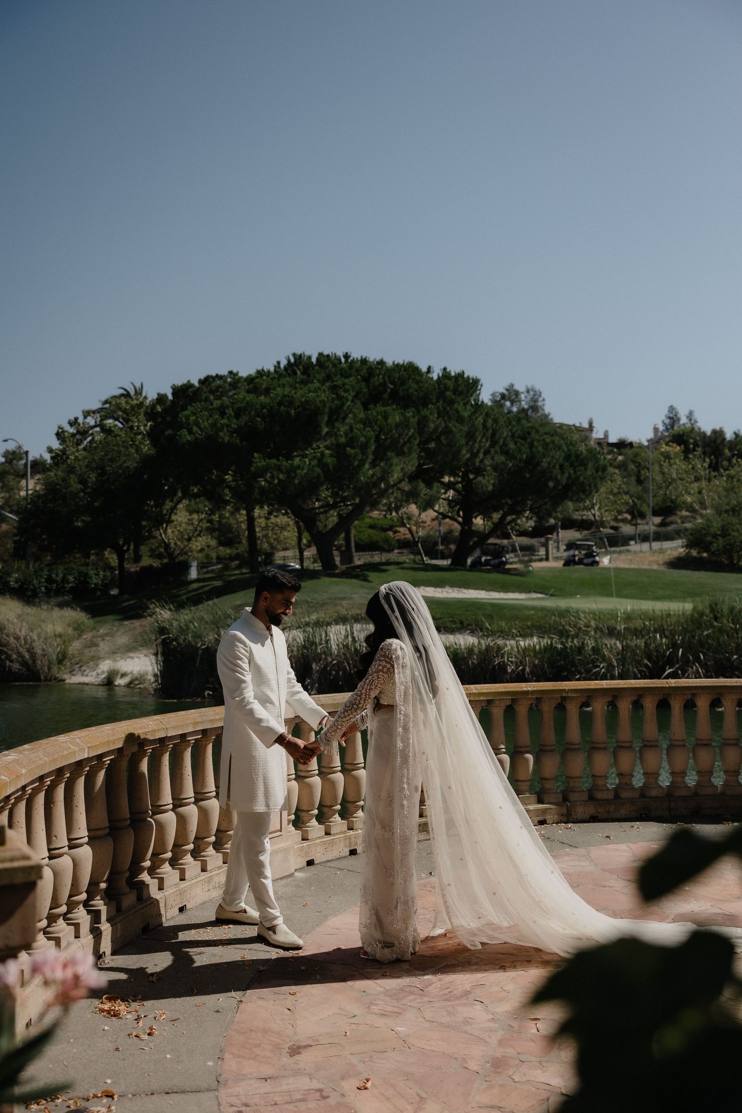 Bride and groom hold hands on a balcony overlooking a lush green golf course on their wedding day.