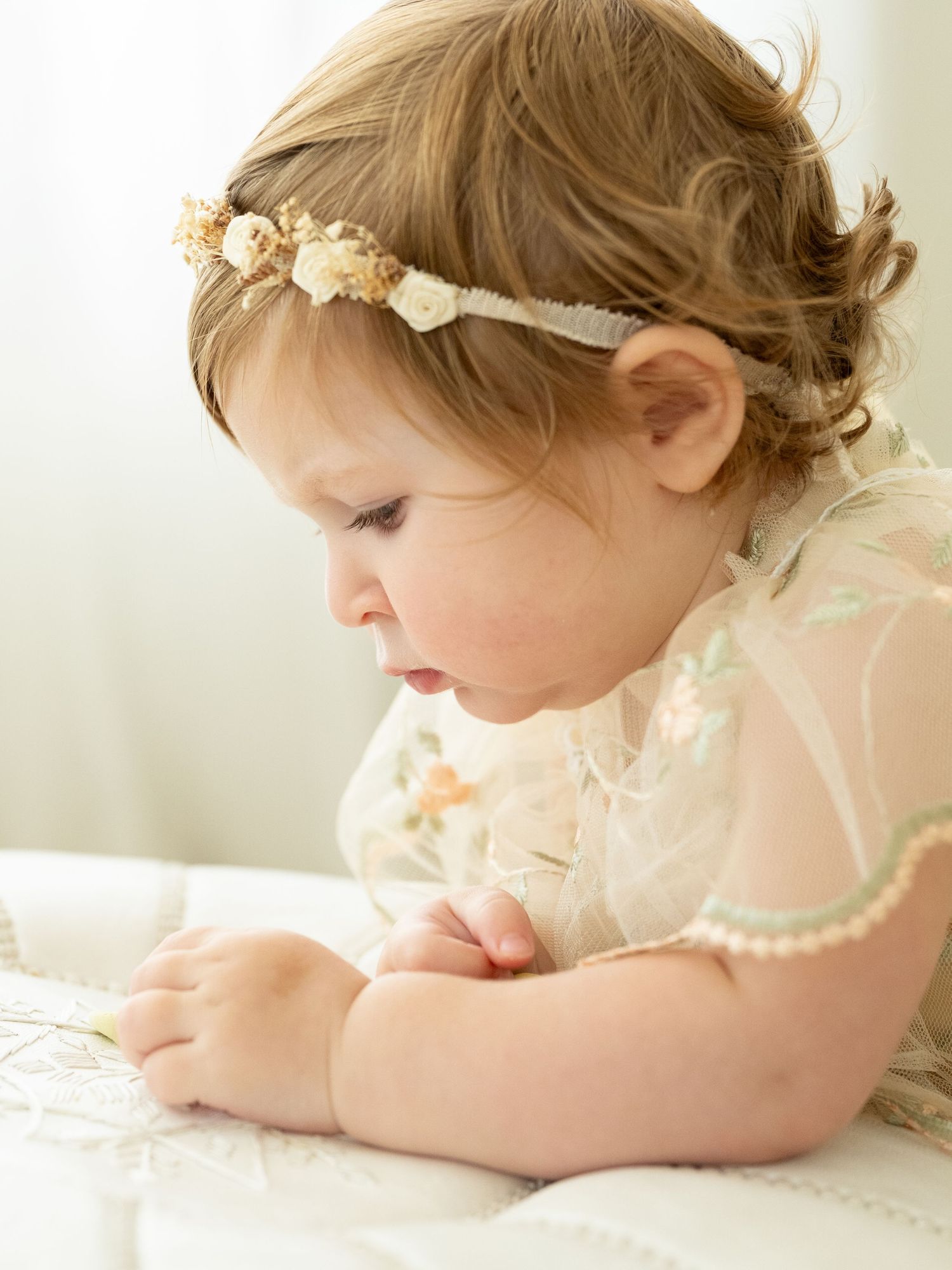 Adorable baby girl with blue eyes wearing a floral gold crown headband and cream tulle dress.