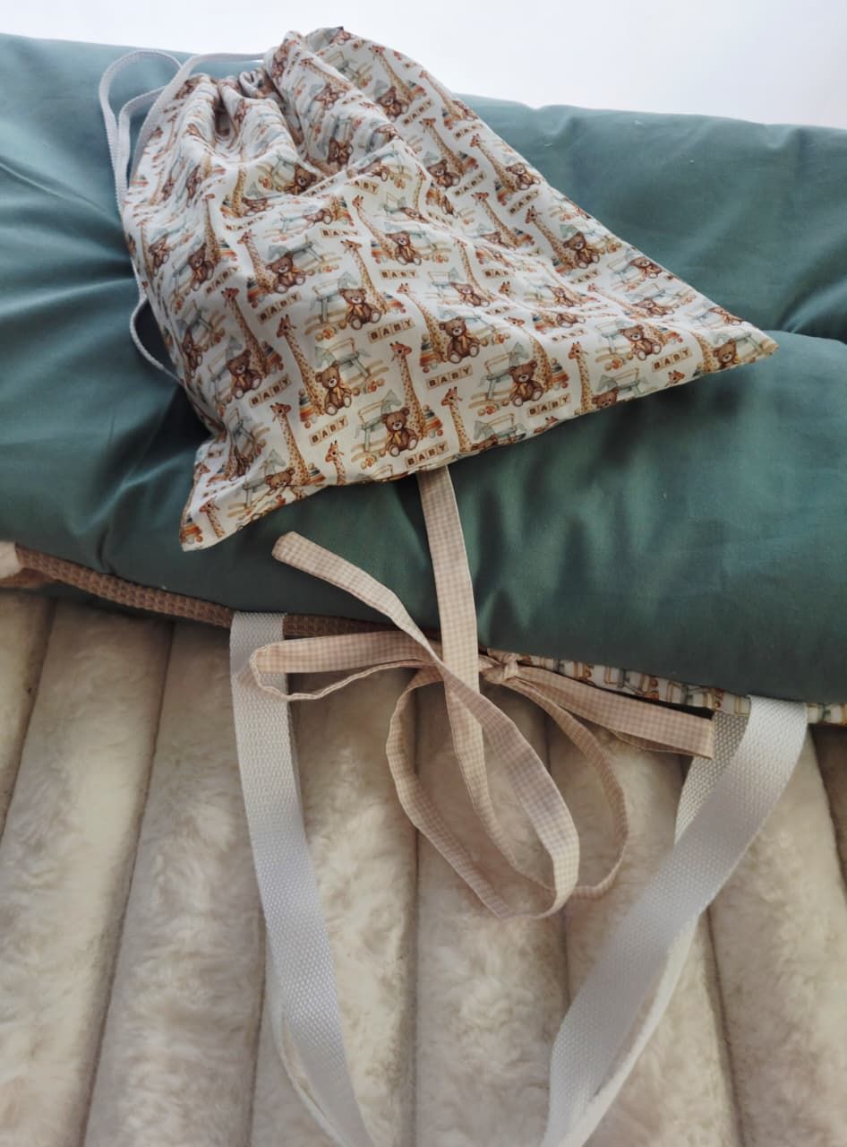 Teal green crib bumper pad set with cream ruffled skirt and a small decorative drawstring bag with bear print fabric.