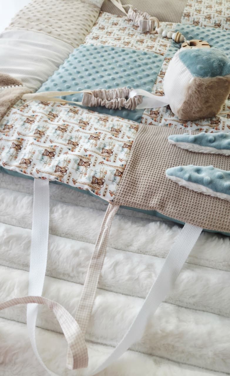 Stacked baby blankets and quilts in soft blue, beige, and white tones with woodland animal prints and ribbon ties.