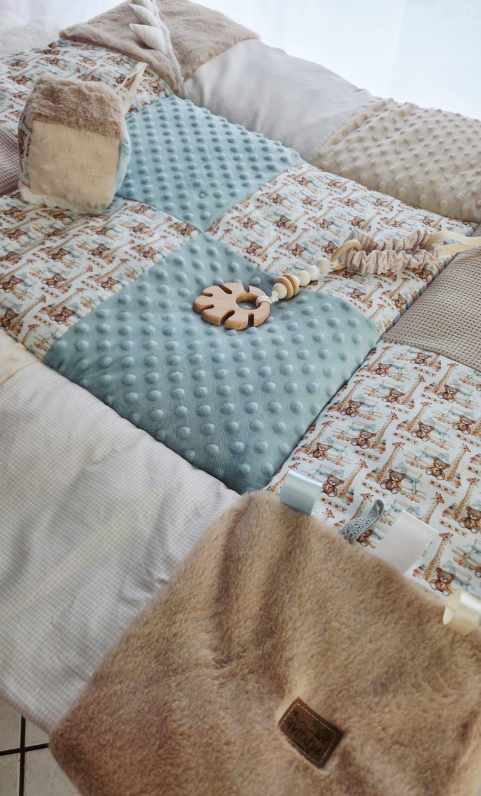 Handmade patchwork baby play mat with minky dots, safari print, and beige teddy fabric, featuring a wooden teething toy.