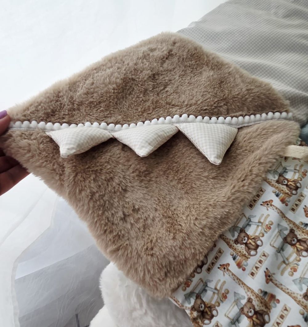 Soft tan faux fur baby blanket with white pom-pom trim and bunting detail, paired with a giraffe print fabric.