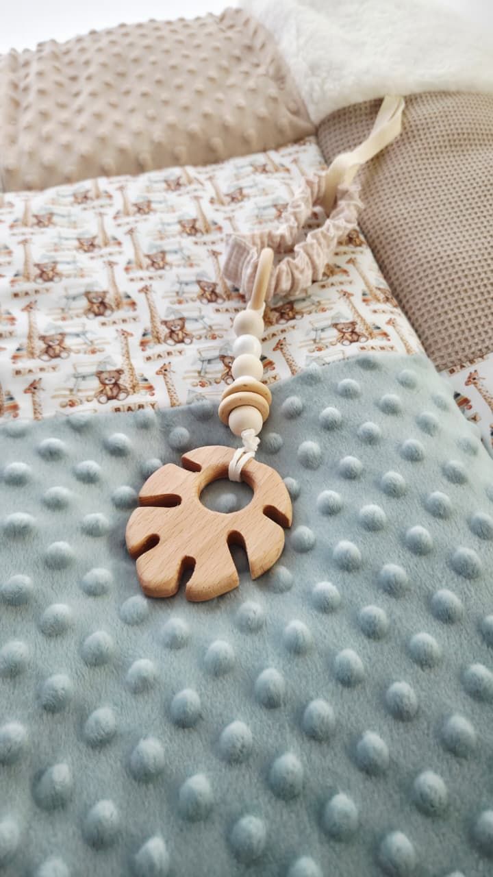 Wooden monstera leaf teething toy with silicone beads on soft minky dot baby blanket.