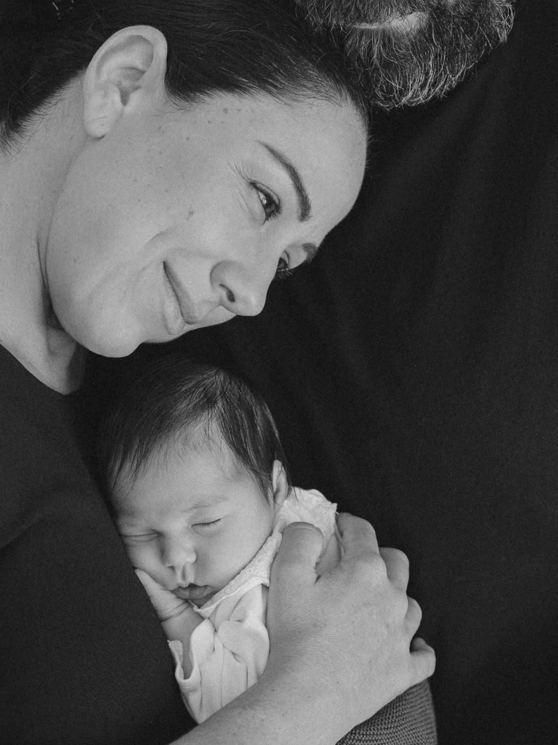 Retrato en blanco y negro de un padre sosteniendo tiernamente a un bebé recién nacido dormido.