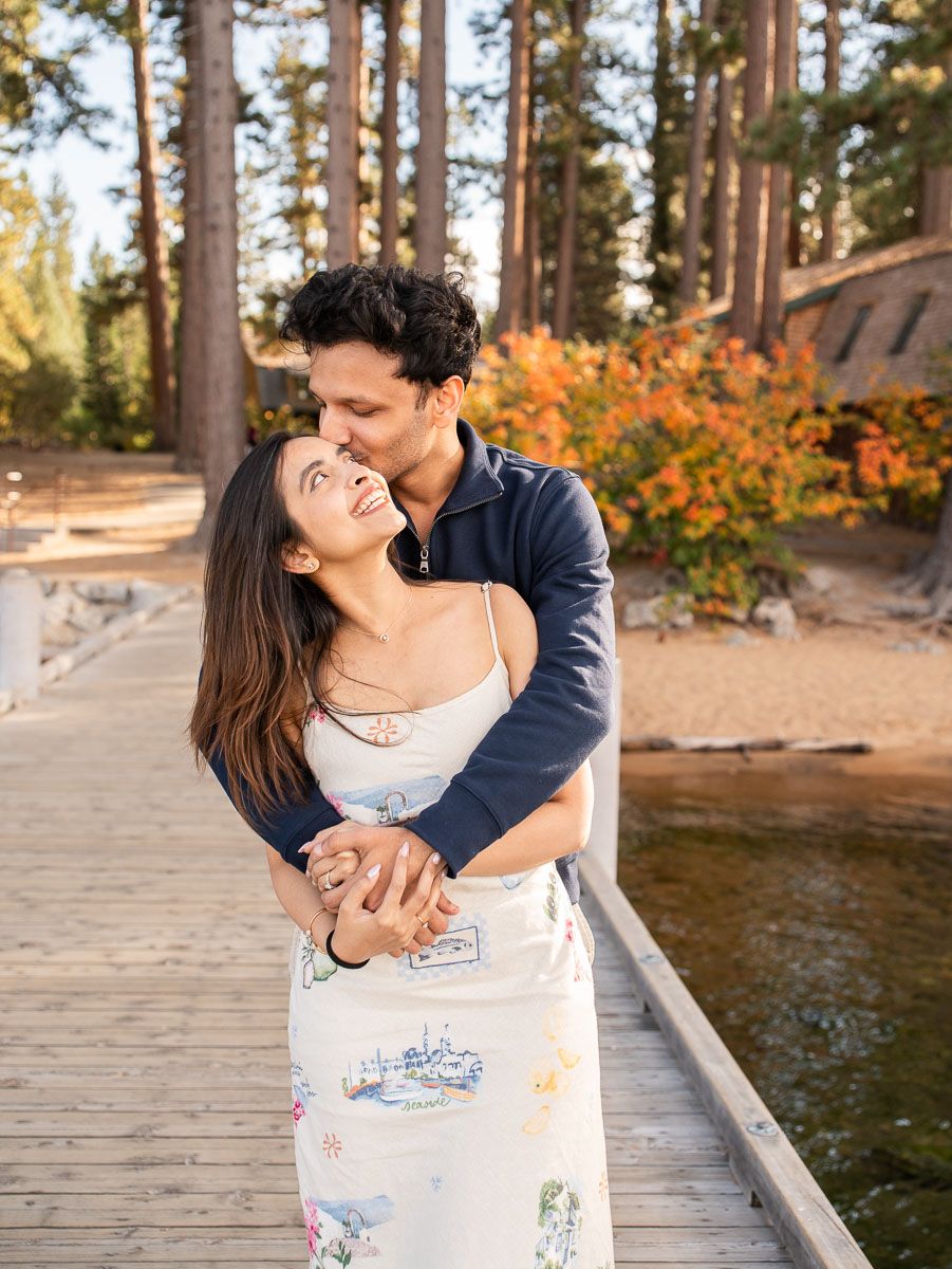 Couple embracing on a lakeside dock surrounded by autumn trees at golden hour.