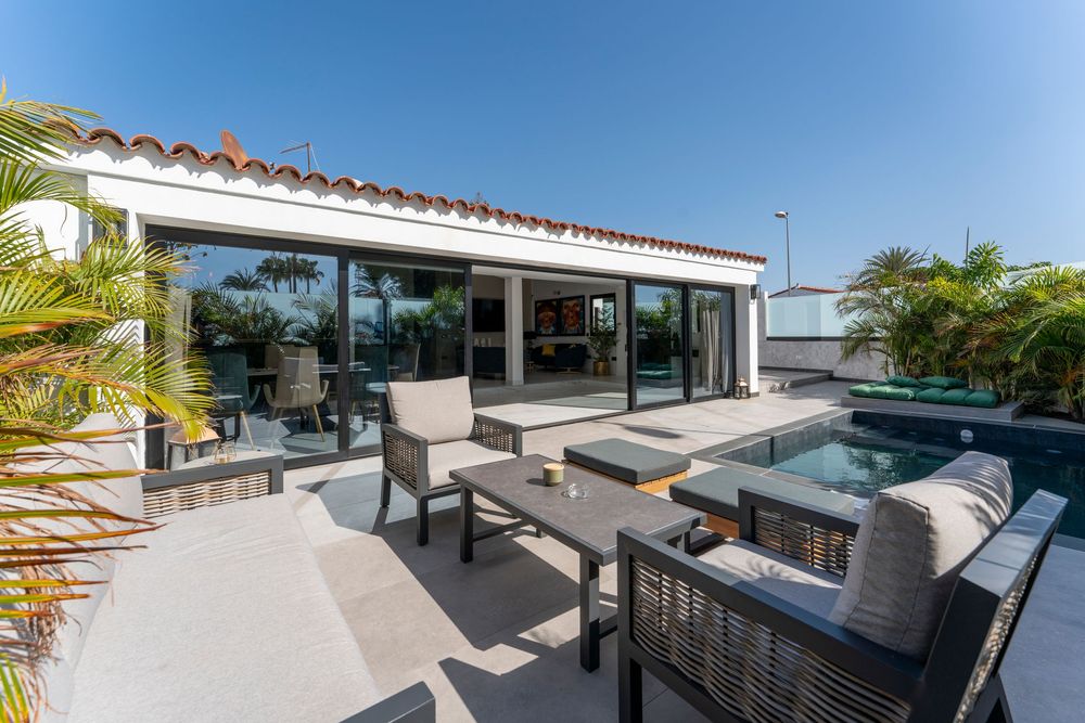 Luxury outdoor patio with pool, hot tub, modern furniture, and large glass doors leading to interior living space.