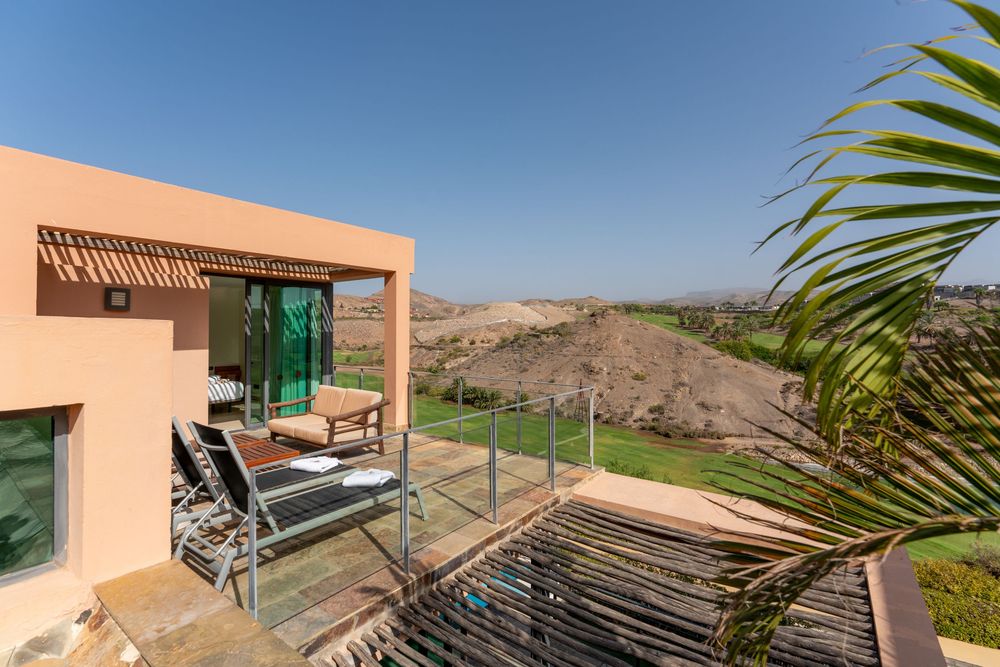 Modern terrace with glass railings overlooking lush golf course and desert hills under clear blue sky.