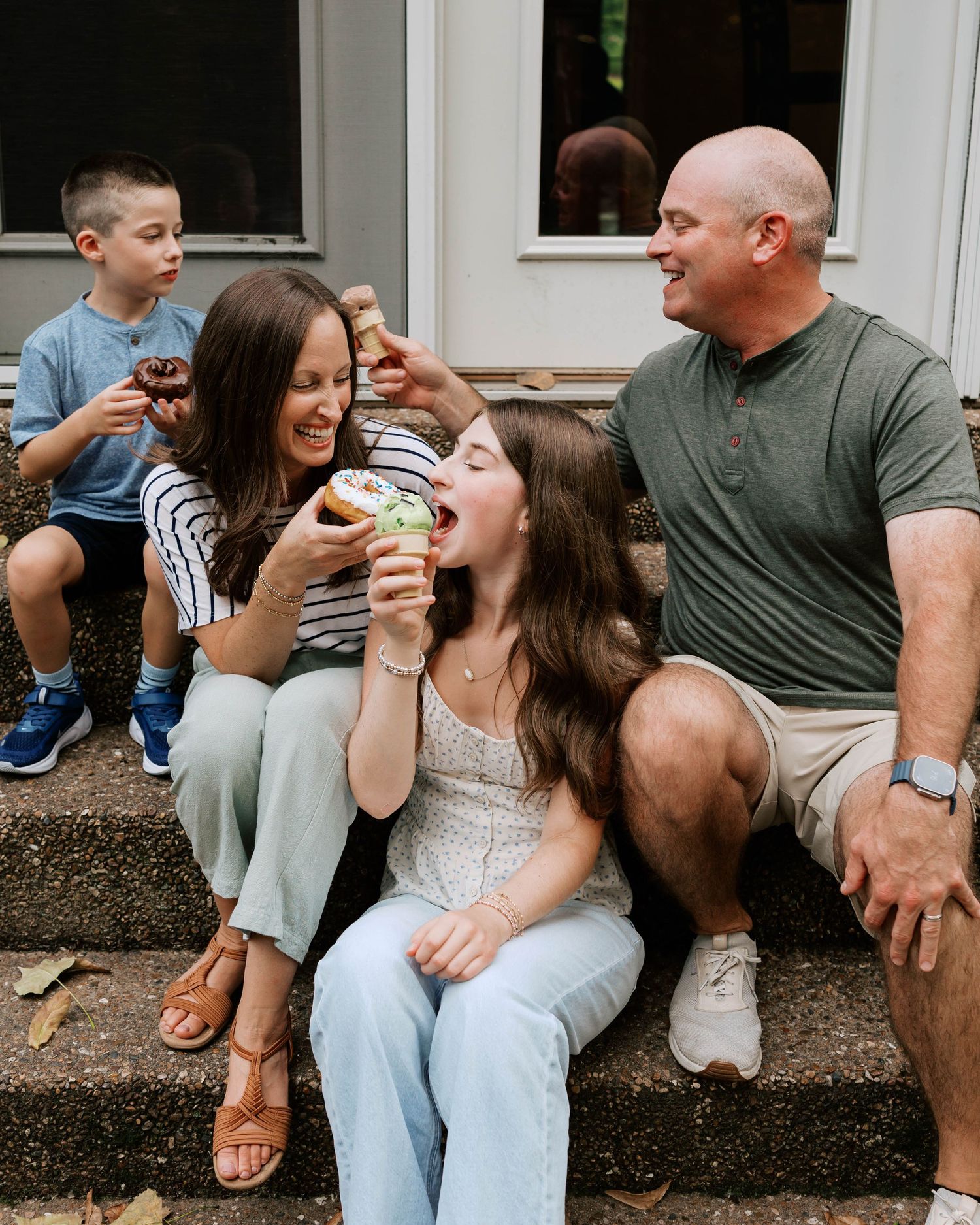 Joyful family of four sitting on steps sharing colorful donuts together outdoors.