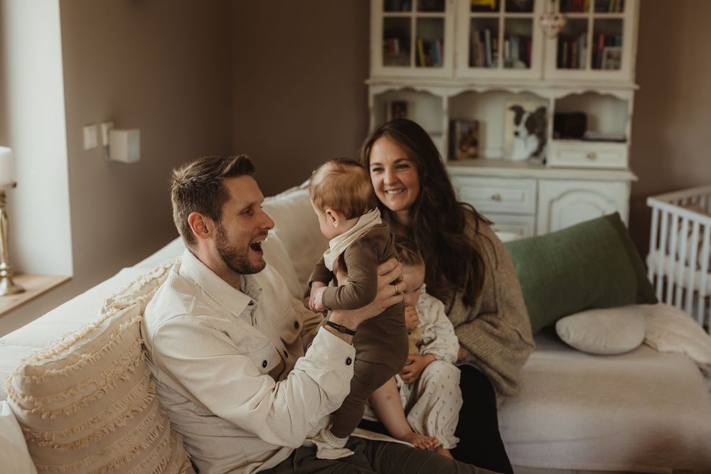 Happy young family with baby sitting on couch in cozy nursery room, sharing joyful moment together.