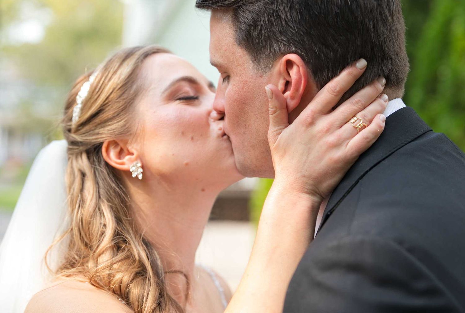 A bride and groom share a romantic first kiss on their wedding day outdoors.